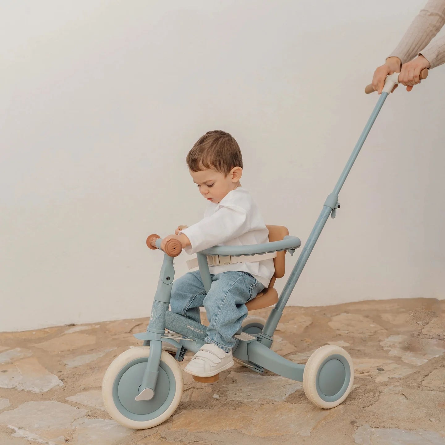 Kind sitzt auf dem Little Dutch Tricycle 4-in-1 in Blau mit Schubstange. Das Schiebedreirad bietet Sicherheit, Komfort und wächst vom Dreirad zum Laufrad für Kinder ab 1 Jahr mit.