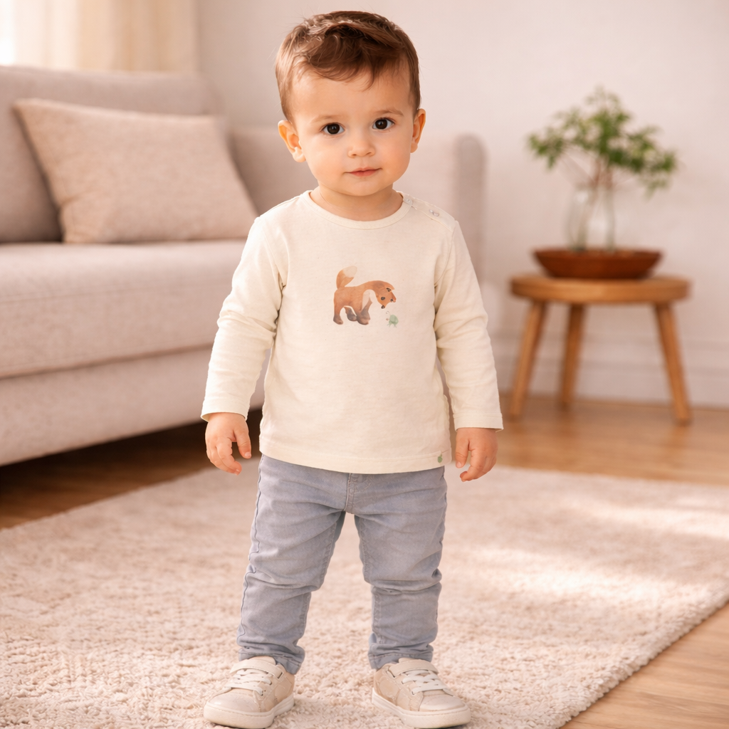 Kleinkind in heller Babybekleidung im Wohnzimmer – Beispiel für Bekleidung, die im 50 % Abverkauf reduziert wird, da sich Schmatzepuffer künftig auf personalisierte Geschenke fokussiert