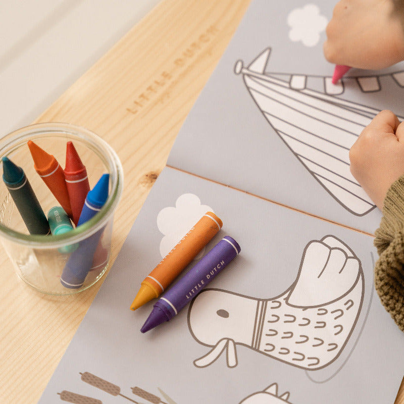 Kind malt mit Wachsmalstiften ein Ausmalbild mit Tiermotiven auf einem Tisch im Kinderzimmer